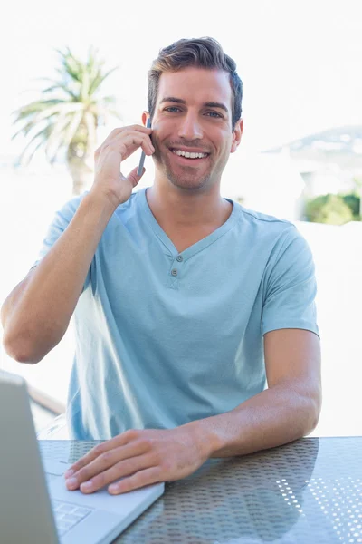 Hombre feliz usando el ordenador portátil y el teléfono móvil —  Fotos de Stock