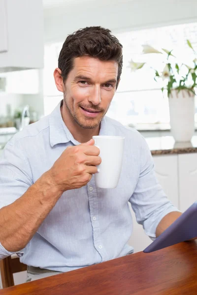 Uomo sorridente utilizzando tablet digitale pur avendo caffè a casa — Foto Stock