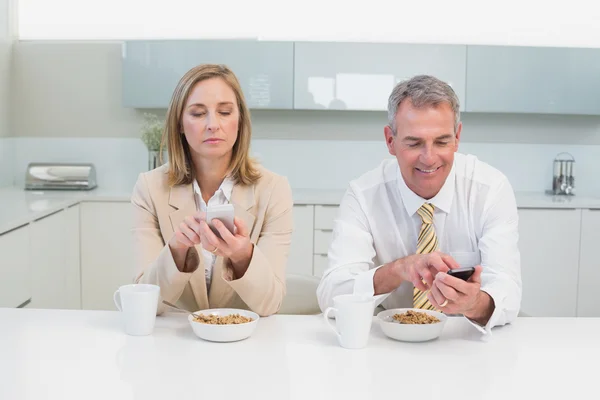 Business couple text messaging while having breakfast in kitchen — Stock Photo, Image