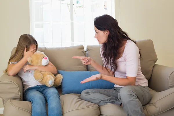 Woman pointing at scared daughter on sofa — Stock Photo, Image