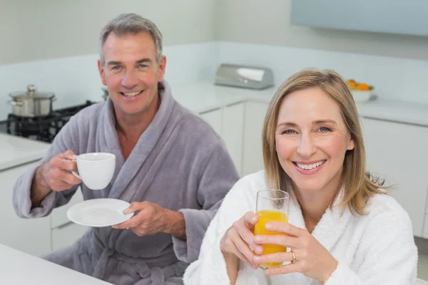 Casal sorridente com suco de laranja e café na cozinha — Fotografia de Stock