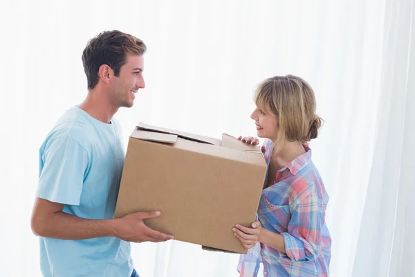 Smiling couple carrying cardboard box in new house — Stock Photo, Image