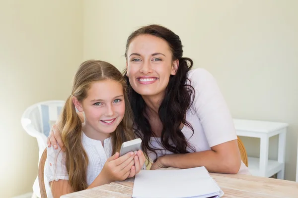 Sorrindo mãe e segurando telefone celular na mesa — Fotografia de Stock