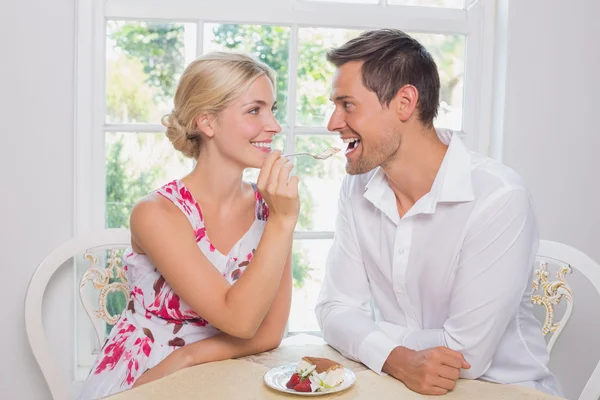 Loving woman feeding man pastry at dining table — Stock Photo, Image