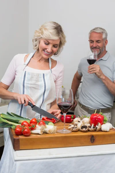 Мужчина с бокалом вина и женщина рубят овощи на кухне — стоковое фото