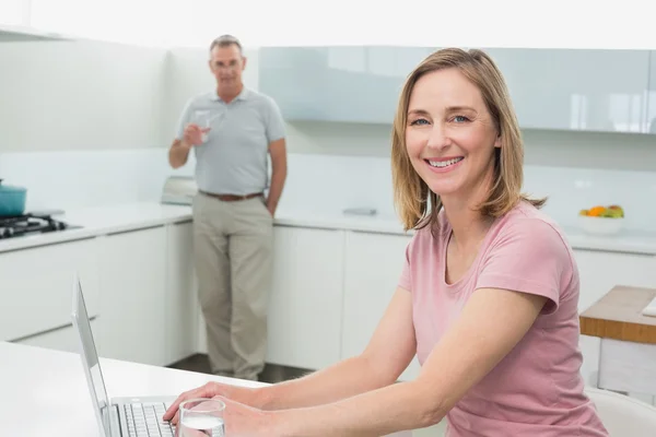 Frau benutzt Laptop, während Mann Wasser in Küche trinkt — Stockfoto