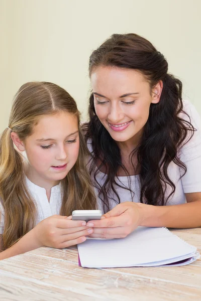 Mother and daughter using mobile phone at table — Stock Photo, Image