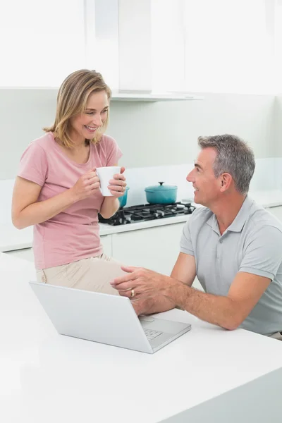 Couple using laptop while woman drinking coffee in kitchen — Stock Photo, Image