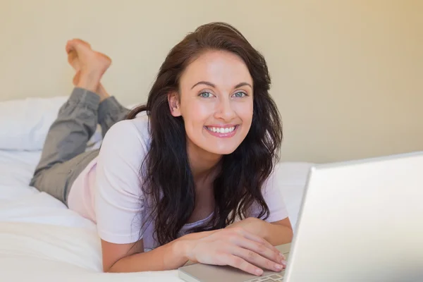 Mutlu bir kadın yatakta yatan bir dizüstü bilgisayar ile — Stok fotoğraf