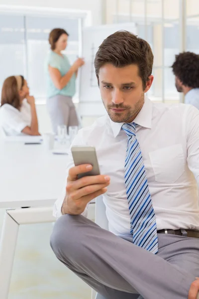 Businessman text messaging with colleagues in meeting Royalty Free Stock Images