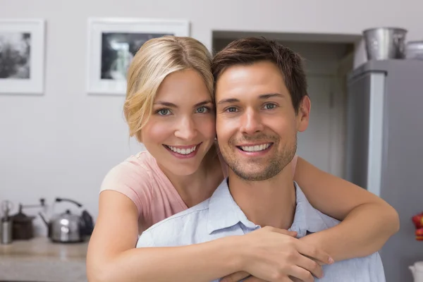 Smiling woman embracing man from behind in kitchen Stock Picture