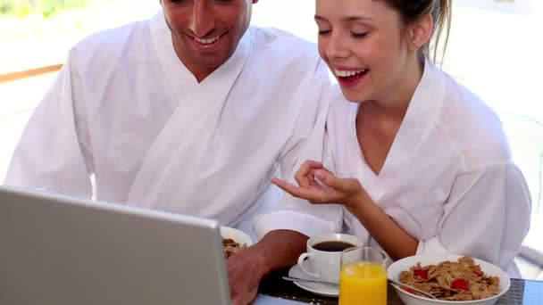 Happy couple having breakfast together looking at laptop — Stock Video