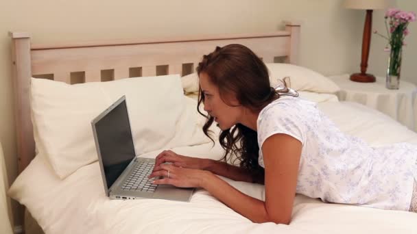 Mooie vrouw liggend op bed met behulp van haar laptop — Stockvideo