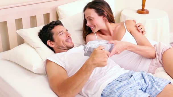 Usmívající se muž dává svou přítelkyni dárek ležící na posteli — Stock video