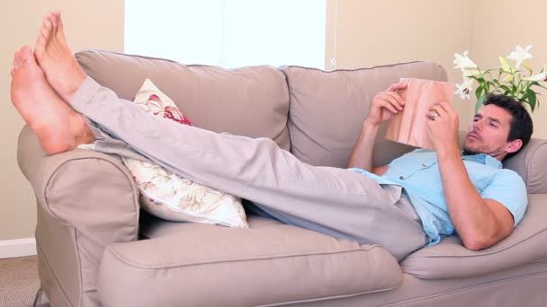 Hombre acostado en el sofá quedarse dormido mientras lee — Vídeos de Stock