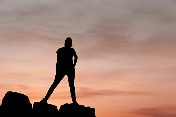 Silhouette einer jungen Frau, die bei Sonnenuntergang auf ein paar Felsen tanzt - horizontal — Stockfoto