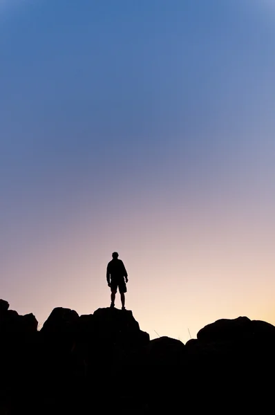 Männersilhouette in der Höhe eines Hügels bei Sonnenuntergang - senkrecht — Stockfoto