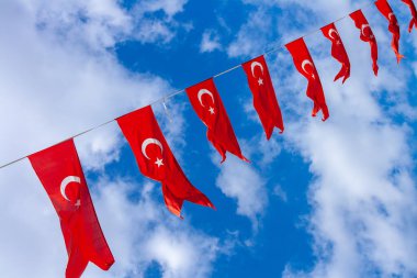 Dar bir ipe bağlı Türk bayrakları, bulutlu mavi gökyüzünün arka planına karşı.