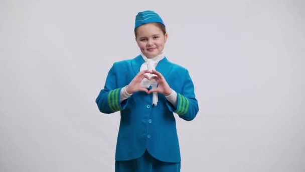 Όμορφο γοητευτικό κορίτσι δείχνει σχήμα καρδιάς με τα χέρια κοιτάζοντας κάμερα χαμογελώντας. Πορτρέτο του χαριτωμένο Καυκάσιος παιδί με στολή αεροσυνοδού θέτοντας την επιλογή της εργασίας του ονείρου. — Αρχείο Βίντεο