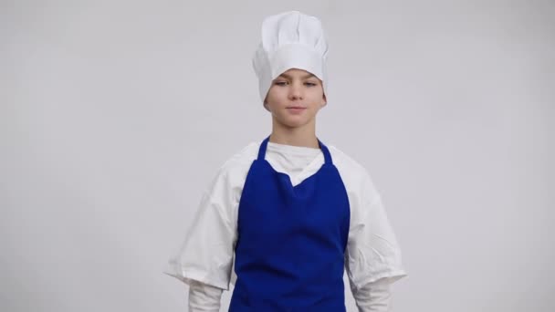 Ontevreden kleine chef-kok in uniform dreigt met rollende pin poseren op witte achtergrond. Portret van een knappe blanke jongen die het kookgereedschap uitrekt en naar de camera kijkt. Culinair en gastronomisch. — Stockvideo