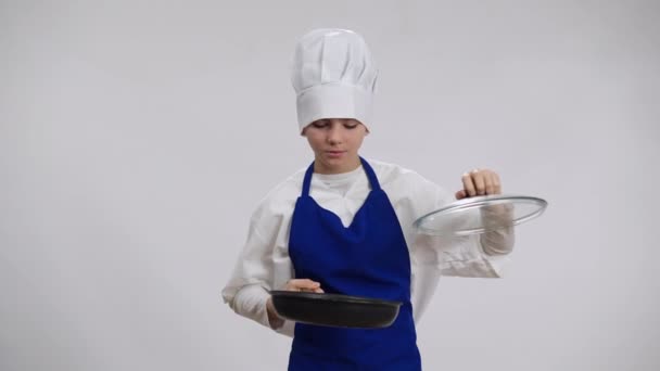 积极自信的小厨师打开煎锅,闻起来像美味的食物,看着镜头,脸上带着自豪的表情.身着厨师帽、围裙、心满意足的白人男孩的背景画像. — 图库视频影像
