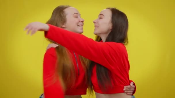 Attractives sœurs jumelles étreignant regardant la caméra posant avec le sourire aux dents sur fond jaune. Heureuse belle mince femmes caucasiennes embrassant et souriant. — Video