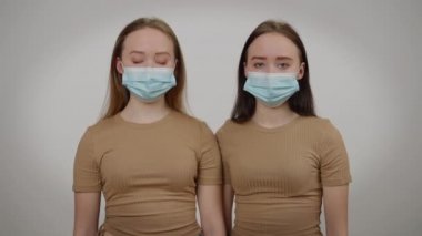 Gri arka planda Covid-19 yüz maskesi takan tek yumurta ikizleri. Kameraya bakan kendine güvenen, güzel, beyaz bir kadının portresi. Koronavirüs salgını olan kardeşler..