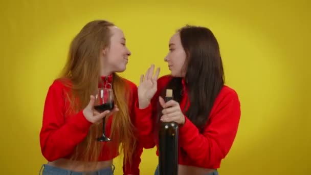 Позитивные сестры-близнецы танцуют с бутылкой вина и бокалом напитка на желтом фоне. Портрет расслабленной беззаботной счастливой кавказской девушки, наслаждающейся отдыхом с алкоголем. — стоковое видео