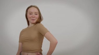 Gri arka planda poz veren muhteşem zayıf, kendine güvenen bin yıllık bir kadın. Kafkasyalı güzel bir kadının portresi. Makyajın solunda kameraya bakıp gülümsüyor. Kadınlık ve güven kavramı.