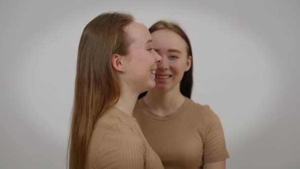 Lachende junge Frau posiert mit Zwillingsschwester im Hintergrund. Positiv glücklich entspannt kaukasischen identischen Frauen lächeln Spaß vor grauem Hintergrund. — Stockvideo