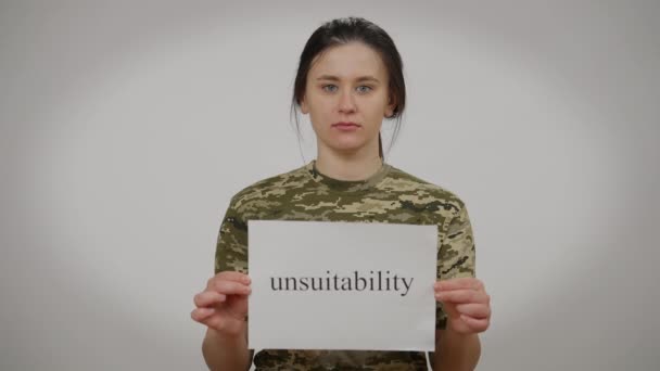 Triste femme stressée en T-shirt kaki posant avec message d'inaptitude à fond gris. Portrait d'une recrue caucasienne bouleversée regardant la caméra. Inégalité et stéréotypes de genre. — Video