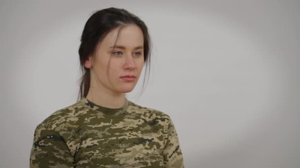Femme millénariste concentrée en T-shirt kaki imitant le tir au pistolet avec les mains gesticulant soufflant tournant en regardant la caméra. Portrait de femme courageuse confiante soldat caucasien posant sur fond gris. — Video