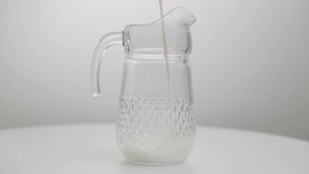 Brocca di vetro da primo piano con latte sano bianco versato al rallentatore. Contenitore per liquidi con latticini. Concetto di cibi sani e bevande ricche di nutrienti di calcio. — Video Stock
