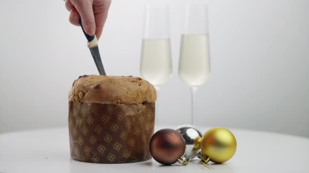 Primer plano de pan de Navidad con joven hembra corte a mano pastelería tradicional. Mujer irreconocible rebanando dulce postre delicioso en vacaciones con dos copas de champán de pie en el fondo. — Vídeos de Stock