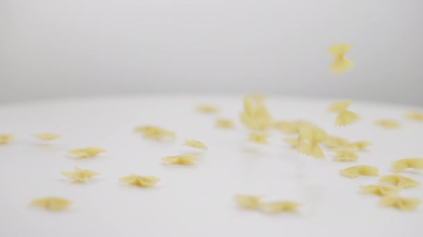 Pâtes crues farfalle tombant sur la table au ralenti au fond blanc. Savoureux plat italien traditionnel non cuit à l'intérieur. Concept de cuisine et culinaire. — Video