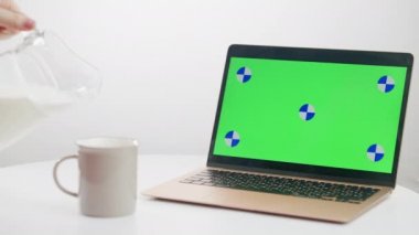 Kromakey dizüstü bilgisayarı masada dururken, sütü yavaş çekimde bardağa dolduruyorum. Tanımlanamayan beyaz kadın yeşil ekran cihazıyla internette sörf yaparak sağlıklı içecek hazırlıyor..