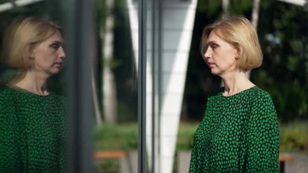 Side view selvsikker kvinde ser på refleksion i glasvæg dreje forlader i slowmotion. Slank attraktiv kaukasiske dame i grøn kjole gå væk i byen. Begrebet tillid og kvindelighed. – Stock-video