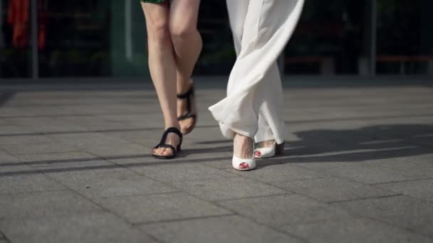 Gambe di donne felici che camminano e ballano al rallentatore sulla soleggiata strada urbana della città. Due irriconoscibili caucasico adulto sottile signore alla moda divertirsi passeggiando all'aperto. Stile di vita e relax. — Video Stock