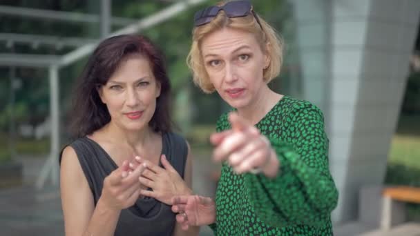 Porträtt av två kvinnor som pratar när de vänder sig mot kameran och hånar i slow motion. Skrattande hånande vuxna vita vänner utomhus på stadens gata. Begreppet antisocialt beteende. — Stockvideo