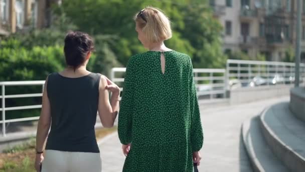 Visszapillantás két nő sétál a város utcáján lassított felvételen mosolyogva. Pozitív boldog kaukázusi barátok sétálnak a szabadban beszélgetni. Hétvégi koncepció. — Stock videók