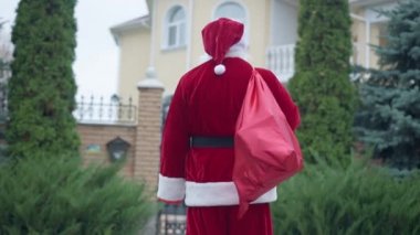 Arka manzara Noel Baba, hediye çantasıyla evin önünde dikilip etrafa bakıyor. Noel Baba 'nın hediye arama adresi. Yeni yıl tatili mevsimi konsepti.