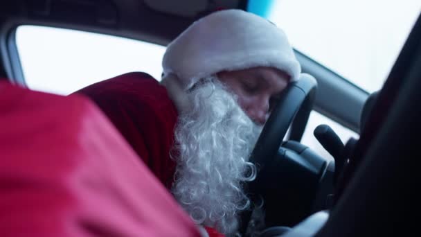 Tired Santa sleeping in car leaning head on steering wheel. Portrait of young exhausted Caucasian man in red costume napping in automobile on New Years eve. Christmas holidays and tiredness concept. — Stock Video