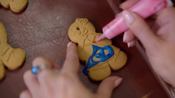 Galleta de Navidad dulce tradicional de cerca con manos caucásicas femeninas que decoran el postre con glaseado real colorido. La mujer irreconocible que cocina en la víspera de Año Nuevo en casa. — Vídeos de Stock