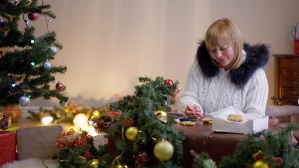 Glimlachende charmante vrouw decoreren peperkoek koekjes op kerstavond binnen thuis. Portret van vrolijke positieve blanke dame bereidt zoet dessert op oudejaarsavond in de woonkamer. — Stockvideo