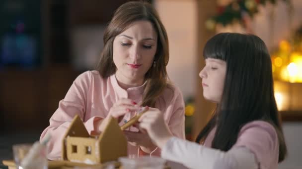 Vakker, hvit kvinne og pen jente som snakker hjemme og lager ingefærmat på nyttår i stua. Lykkelig, ung mor og søt datter som nyter familiefritid på julaften. – stockvideo
