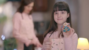 Mutfakta arka planda bulanık bir kadınla böbürlenen tatlı bir kız. Mutlu beyaz kızın portresi Noel 'de tatlı pişirmeye yardım ediyor..