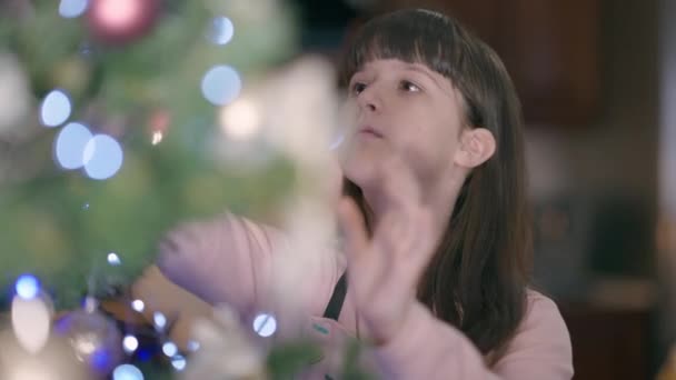 Retrato de chica linda admirando árbol de Navidad decorado en casa con la mujer borrosa en el fondo. Feliz encantadora hija caucásica decorando la casa en la víspera de Año Nuevo en el interior. — Vídeos de Stock