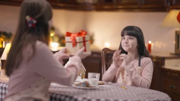 Aufgeregt kleine Tochter erhält Weihnachtsgeschenk an Silvester von Mutter. Porträt eines begeisterten kaukasischen Mädchens beim Öffnen einer Geschenkschachtel mit erstauntem Gesichtsausdruck, das mit einer Frau am Tisch sitzt. — Stockvideo