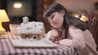 Mutfakta oturmuş, dekore edilmiş zencefilli kurabiyeye hayran olan mutlu, güzel bir kız. İçeride Noel 'i bekleyen neşeli beyaz çocuğun portresi. Yeni yıl kutlamaları gelenekleri.