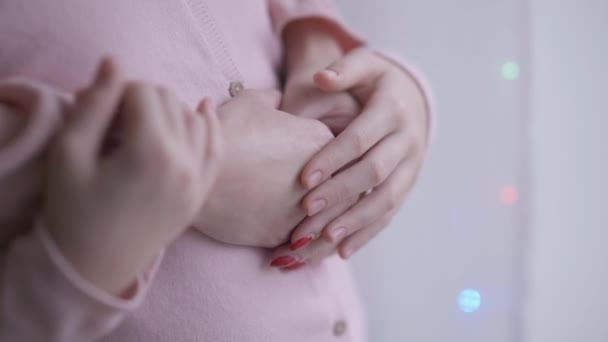 Close-up unrecognizable girl hands caressing woman palms with Christmas lights flashing indoors. Little Caucasian daughter and young mother holding hands hugging standing at window at home on New Year — Stock Video